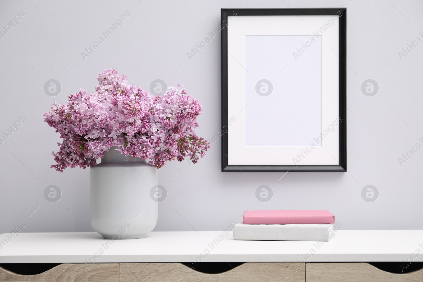 Beautiful lilac flowers in vase, books and picture frame indoors Photo of Beautiful lilac flowers in vase, books and picture frame indoors