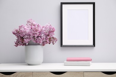 Photo of Beautiful lilac flowers in vase, books and picture frame indoors