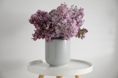 Photo of Beautiful lilac flowers in vase on table near white wall indoors