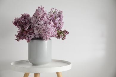 Photo of Beautiful lilac flowers in vase on table near white wall indoors, space for text