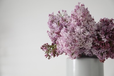 Photo of Beautiful lilac flowers in vase near white table, closeup. Space for text