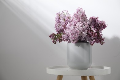 Photo of Beautiful lilac flowers in vase on table near white wall indoors, space for text