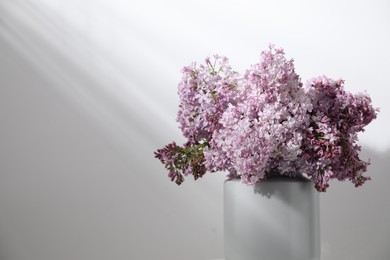Photo of Beautiful lilac flowers in vase near white table, closeup. Space for text