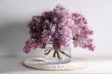 Photo of Beautiful lilac flowers in glass vase on table near white wall indoors