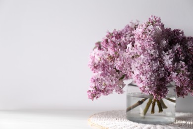 Photo of Beautiful lilac flowers in glass vase on table near white wall indoors, closeup. Space for text