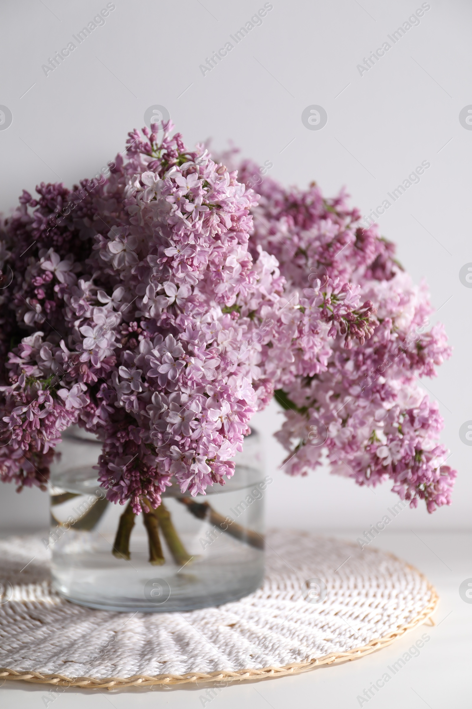 Beautiful lilac flowers in glass vase on table near white wall, closeup Photo of Beautiful lilac flowers in glass vase on table near white wall, closeup