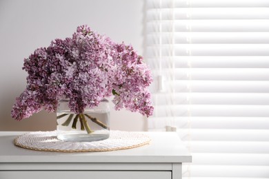 Photo of Beautiful lilac flowers in glass vase on cabinet indoors, space for text
