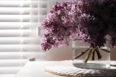 Photo of Beautiful lilac flowers in glass vase on table indoors, closeup. Space for text