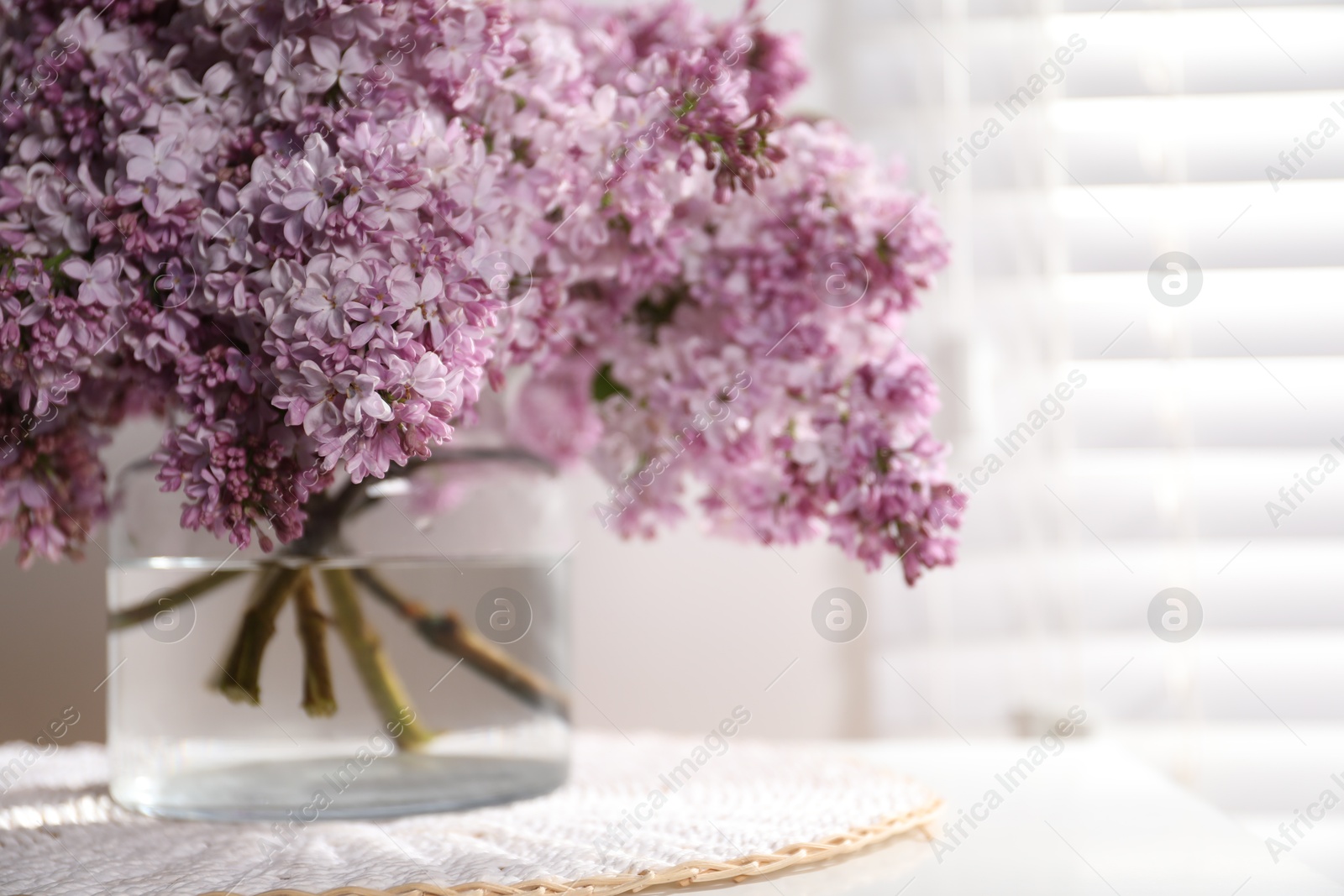 Beautiful lilac flowers in glass vase on table indoors, closeup. Space for text Photo of Beautiful lilac flowers in glass vase on table indoors, closeup. Space for text