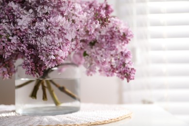 Photo of Beautiful lilac flowers in glass vase on table indoors, closeup. Space for text