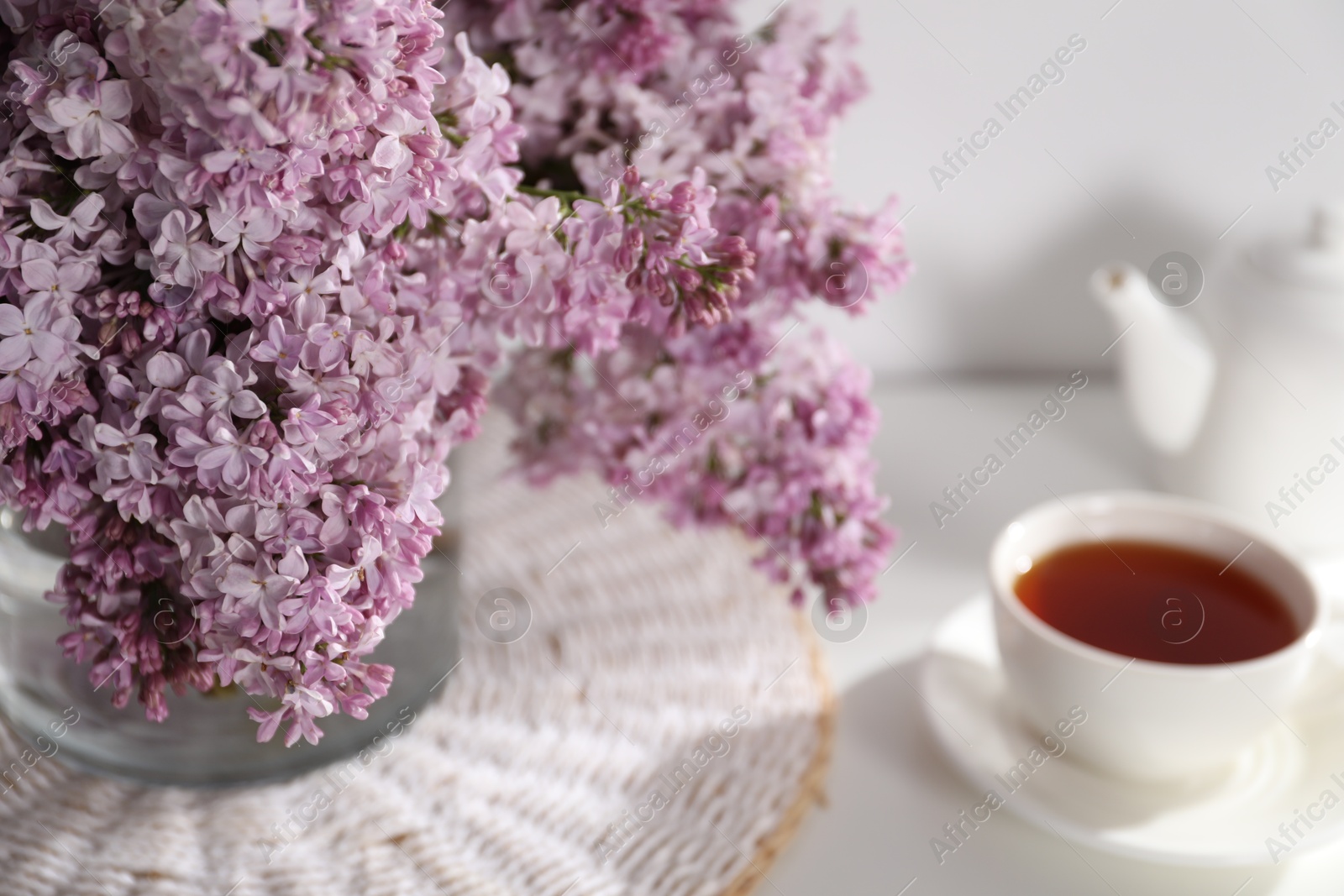 Beautiful lilac flowers in glass vase and tea on table, closeup Photo of Beautiful lilac flowers in glass vase and tea on table, closeup
