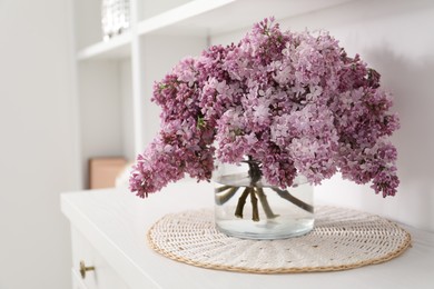 Photo of Beautiful lilac flowers in glass vase on cabinet indoors, space for text