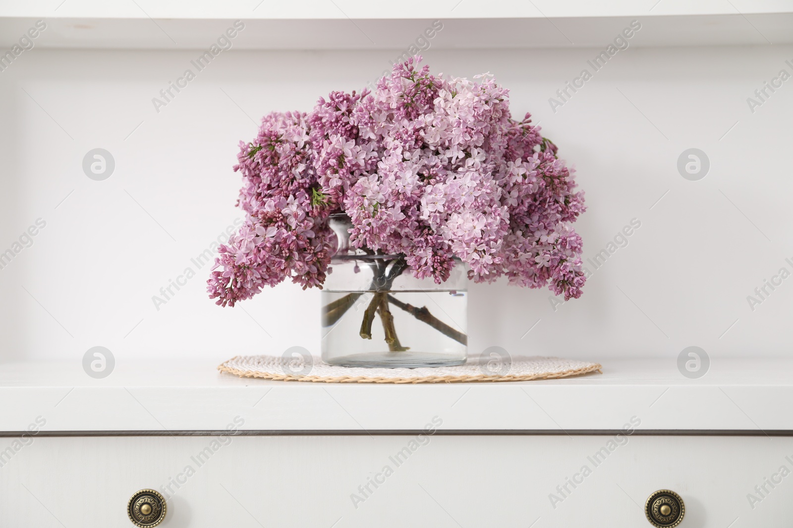Beautiful lilac flowers in glass vase on cabinet indoors Photo of Beautiful lilac flowers in glass vase on cabinet indoors