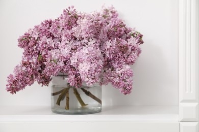 Photo of Beautiful lilac flowers in glass vase on shelf indoors