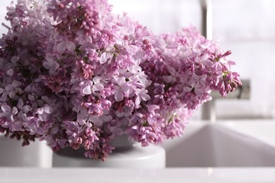 Photo of Beautiful lilac flowers in kitchen sink indoors, closeup