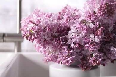 Photo of Beautiful lilac flowers in kitchen sink indoors, closeup