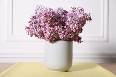 Photo of Beautiful lilac flowers in vase on table near white wall indoors