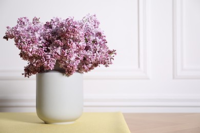 Photo of Beautiful lilac flowers in vase on table near white wall indoors, space for text