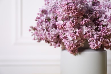 Photo of Beautiful lilac flowers in vase indoors, closeup. Space for text