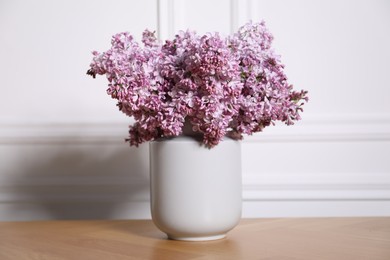 Photo of Beautiful lilac flowers in vase on wooden table near white wall indoors
