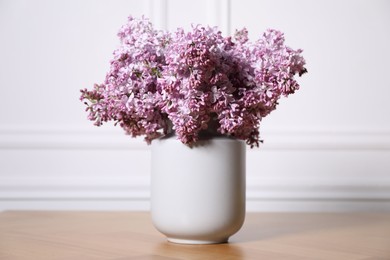 Photo of Beautiful lilac flowers in vase on wooden table near white wall indoors