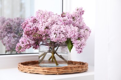 Photo of Beautiful lilac flowers in glass vase on window sill indoors