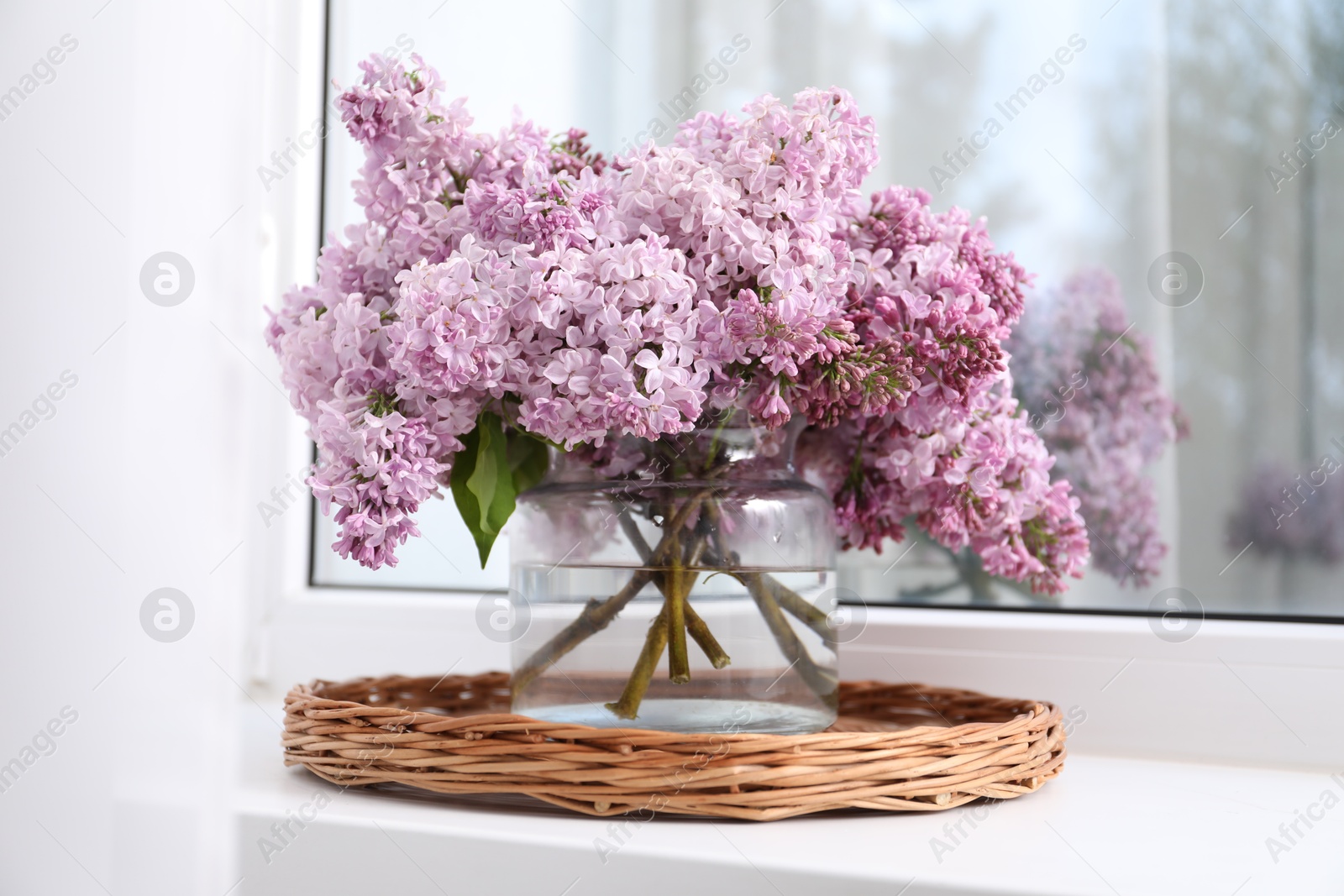 Beautiful lilac flowers in glass vase on window sill indoors Photo of Beautiful lilac flowers in glass vase on window sill indoors