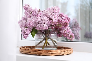 Photo of Beautiful lilac flowers in glass vase on window sill indoors