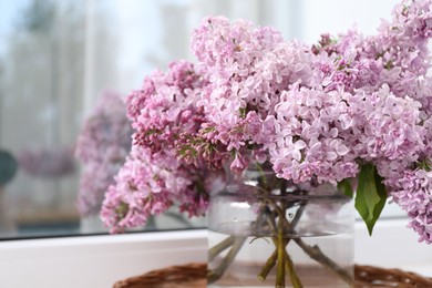 Photo of Beautiful lilac flowers in glass vase on window sill indoors, closeup. Space for text