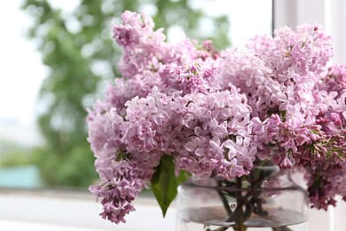 Photo of Beautiful lilac flowers in glass vase near window, closeup. Space for text