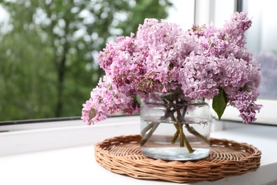 Photo of Beautiful lilac flowers in glass vase on window sill indoors, closeup. Space for text
