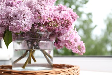 Photo of Beautiful lilac flowers in glass vase on window sill indoors, closeup. Space for text