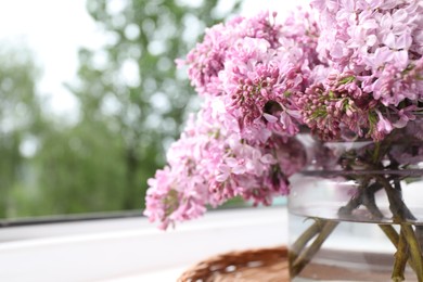 Photo of Beautiful lilac flowers in glass vase on window sill indoors, closeup. Space for text