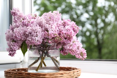 Photo of Beautiful lilac flowers in glass vase on window sill indoors, closeup. Space for text