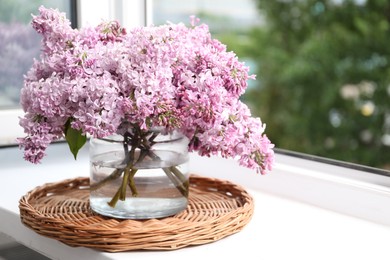 Photo of Beautiful lilac flowers in glass vase on window sill indoors, closeup. Space for text