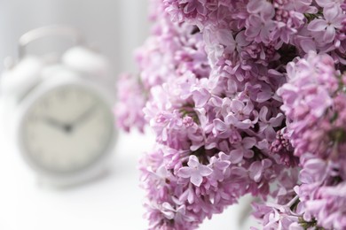 Photo of Beautiful lilac flowers and alarm clock on table indoors, closeup. Space for text