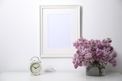 Photo of Beautiful lilac flowers and alarm clock on table near white wall indoors