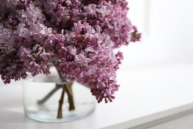 Photo of Beautiful lilac flowers in glass vase on cabinet indoors, closeup. Space for text