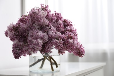 Photo of Beautiful lilac flowers in glass vase on cabinet indoors, space for text