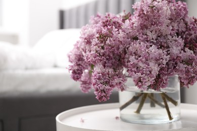 Photo of Beautiful lilac flowers in glass vase on table indoors, closeup. Space for text