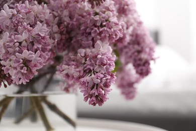 Photo of Beautiful lilac flowers in glass vase on table indoors, closeup. Space for text