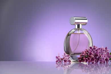 Photo of Beautiful lilac flowers and perfume on mirror surface against violet gradient background, space for text