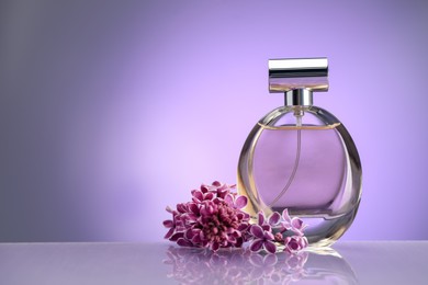 Photo of Beautiful lilac flowers and perfume on mirror surface against violet gradient background, space for text