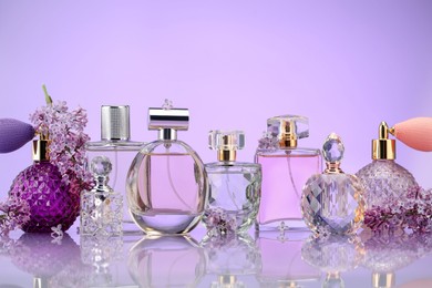 Photo of Bottles of perfume and lilac flowers on mirror surface against violet background