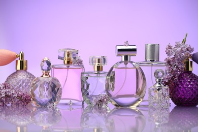 Photo of Bottles of perfume and lilac flowers on mirror surface against violet background