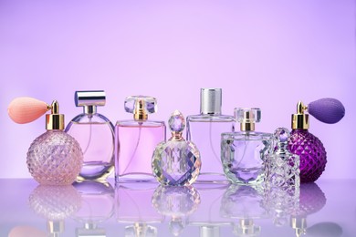 Photo of Bottles of perfume on mirror surface against violet background