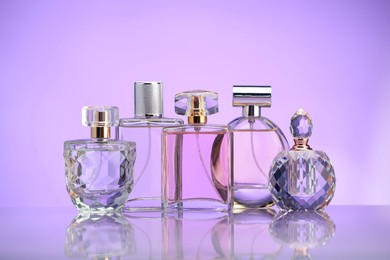 Photo of Bottles of perfume on mirror surface against violet background