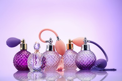 Photo of Bottles of perfume on mirror surface against pale violet gradient background