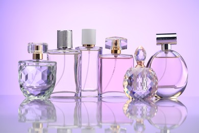 Photo of Bottles of perfume on mirror surface against pale violet gradient background