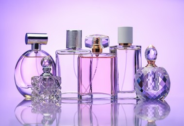 Photo of Bottles of perfume on mirror surface against pale violet gradient background